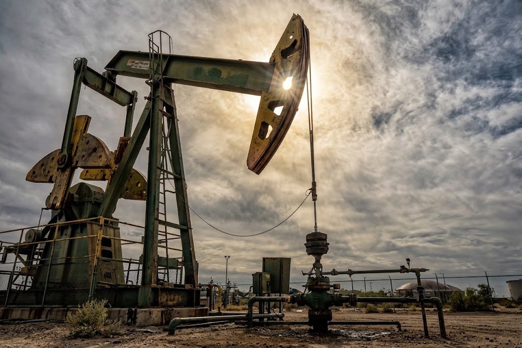 Oil pumpjack silhouette against a dark sky, representing global crude oil markets and falling oil prices